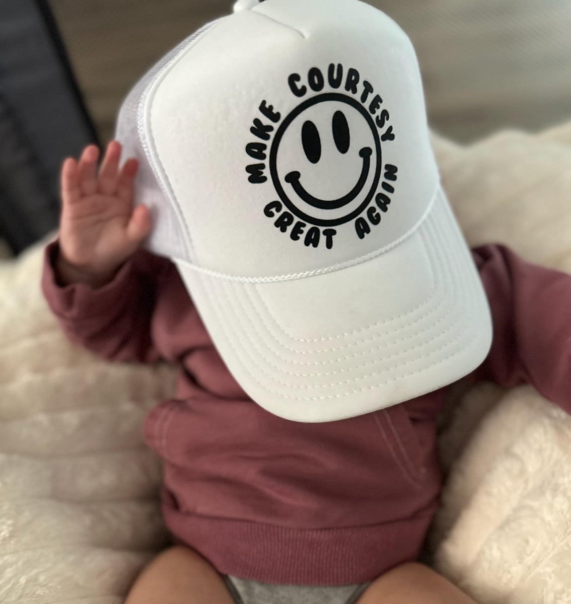 Baby holding a Make Courtesy Great Again trucker hat