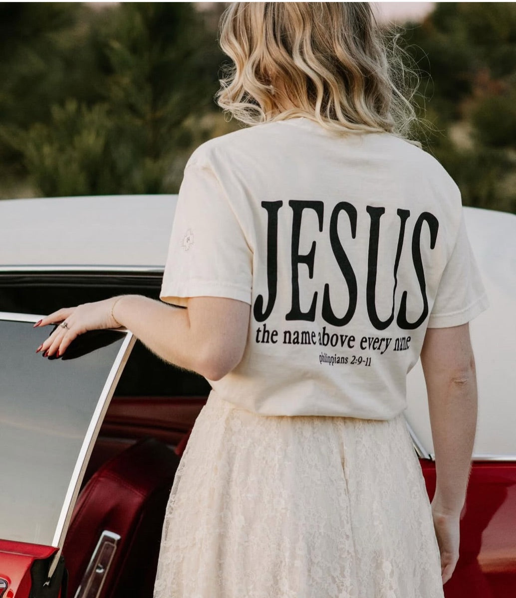 Cream Jesus tee beside a red car